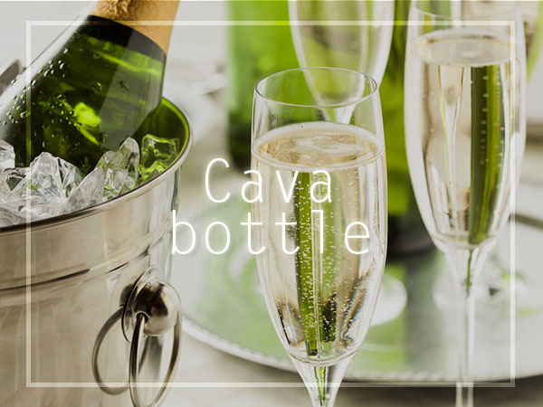 Botella de cava en una cubitera con hielo y dos copas servidas sobre una mesa.